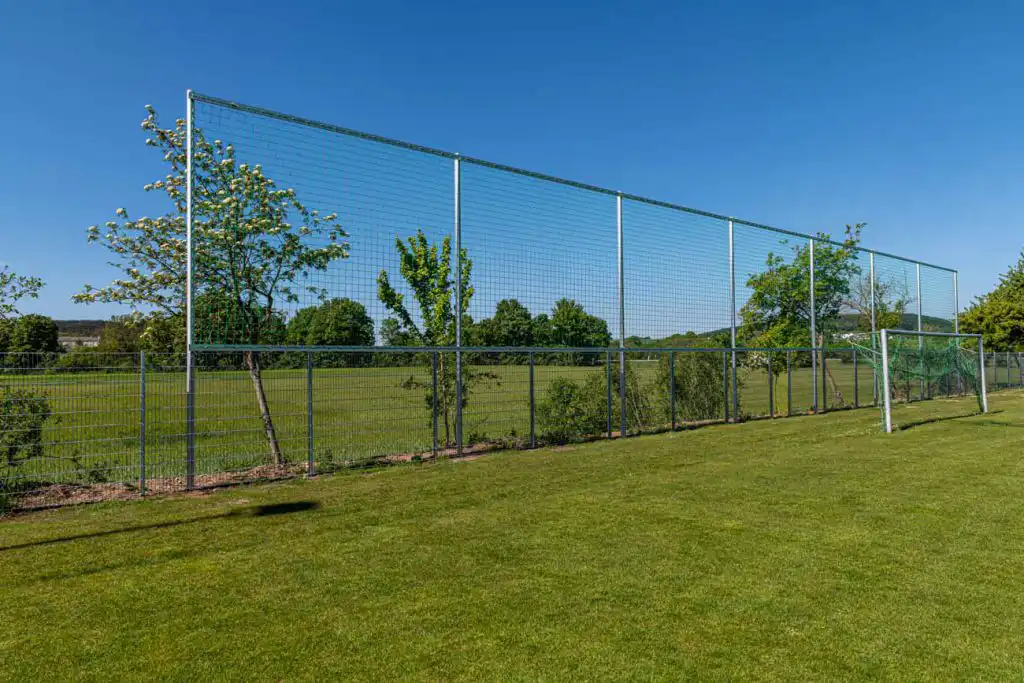 ballfangzaun-hinter-fussballtor Hochwertiger Ballfangzaun hinter einem Fußballtor auf einem Sportplatz.